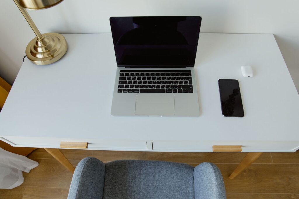 Stylish home office setup featuring a laptop, smartphone, and lamp on a minimalist white desk.